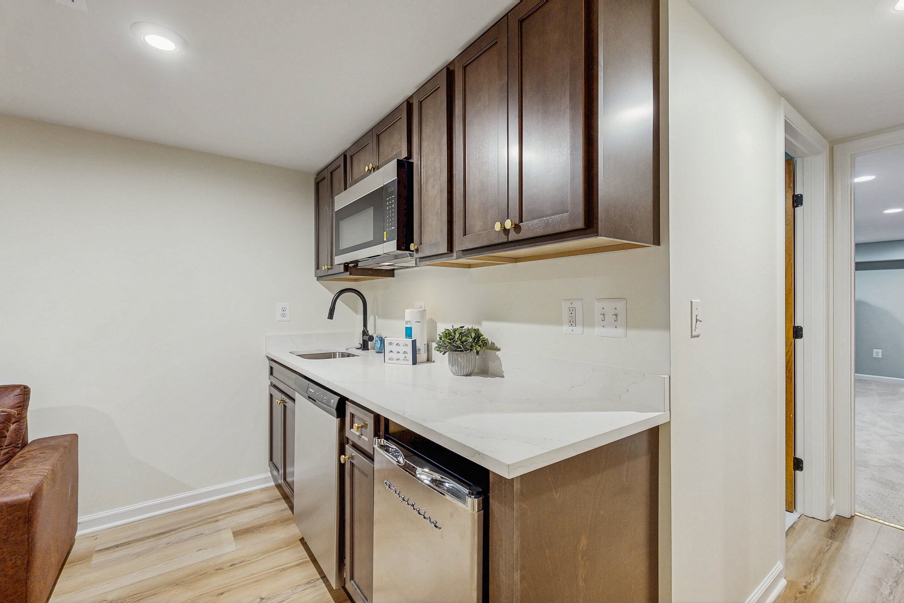 A modern kitchen with dark wooden cabinets, a stainless steel dishwasher, and a white countertop.