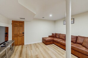 A modern living room with a wooden door, a brown leather sofa, and a wooden cabinet. - Relaxing Lakeside Cabin With Private Dock, Firepit, Boat Ramp and Water Access (Bumpass)
