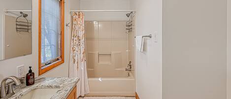 A bathroom with a sink, mirror, shower, and a window with blinds.