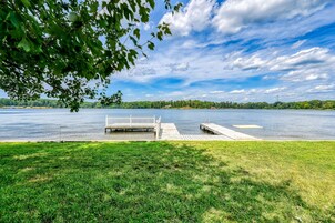 Vista de un lago con un área verde, un muelle de madera y un banco blanco.