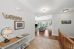 Un interior moderno con un cartel de 'Welcome', una cita enmarcada, una lámpara antigua, una consola de madera y una escalera.