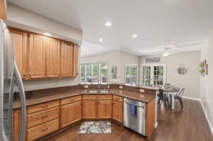 Una cocina con armarios de madera, un refrigerador de acero inoxidable, un lavavajillas y una zona de comedor con una mesa y sillas.