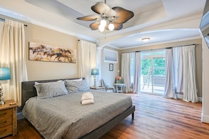 Ein Schlafzimmer mit einem großen Bett, einem Deckenventilator, einem Gemälde, einem Schreibtisch und Blick ins Freie.