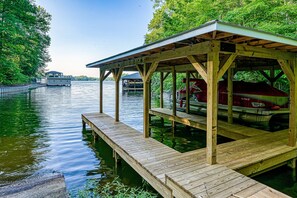 A wooden dock extending into a calm lake, with a covered seating area and a boat docked nearby. - Renovated Lakehouse With Dock, hot Tub, Firepit & Bi-level Deck - Dogs OK (Mineral)