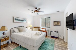 Una camera da letto con un letto, una scrivania, una sedia, un ventilatore a soffitto e opere d'arte alle pareti.