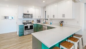 Uma cozinha moderna com armários brancos, uma ilha central com banquetas, forno embutido e micro-ondas.