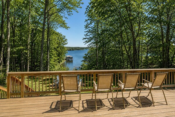 A wooden deck with chairs overlooking a lake, surrounded by trees. - Renovated Lakehouse With Dock, hot Tub, Firepit & Bi-level Deck - Dogs OK (Mineral)