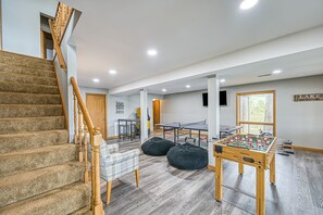 Ein geräumiger Raum mit einer Holztreppe, einem Kicker, einem Tischtennisplatte und einem großen Fenster mit der Aufschrift 'SEE'.