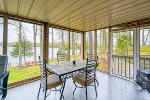 A covered outdoor seating area with a table and chairs, large windows, and a view of a lake. - Lovely Lakefront Home With Private Brand-new Dock, Game Room, Beach, Boat Access (Mineral)