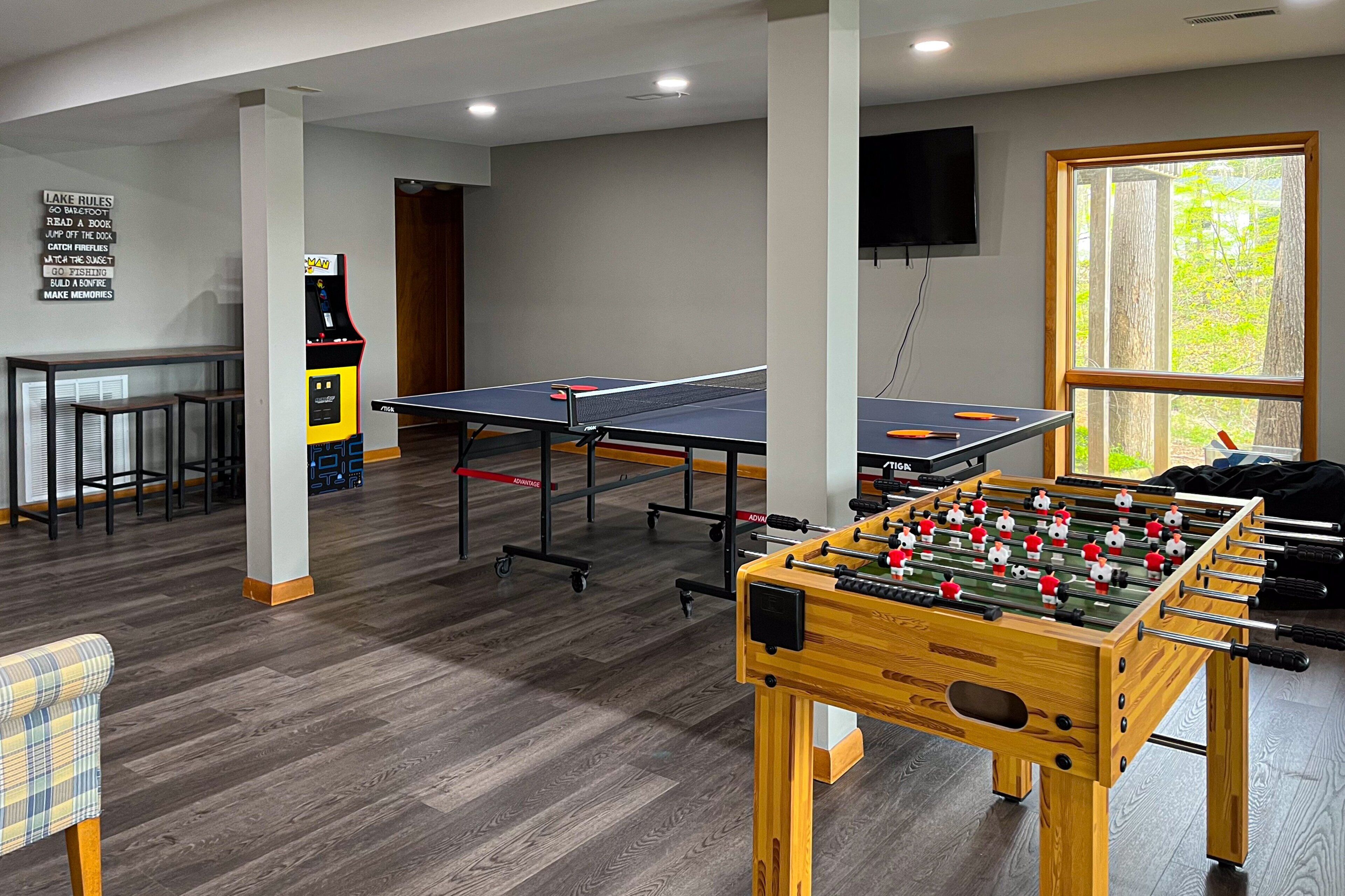 A room with a foosball table, ping pong table, and a foosball table in the corner.