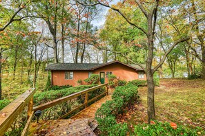 A cabin with a wooden deck, surrounded by trees and a small garden. - Lovely Lakefront Home With Private Brand-new Dock, Game Room, Beach, Boat Access (Mineral)