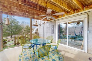 Un patio techado con mesa y sillas de vidrio, un ventilador de techo y vistas al exterior.