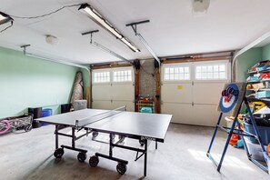 A spacious indoor area with a ping pong table, ceiling lights, and a shelving unit with various items. - Nature Lover's Lakefront Home With a Beach, Dock, Fire Ring, & More (Orange)