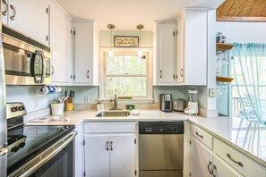 A kitchen with white cabinets, a stainless steel dishwasher, a microwave, and a window with a view of trees. - Secluded Lakefront Home W/private Beach, Deck, gas Grill, Firepit, Lake Views (Bumpass)