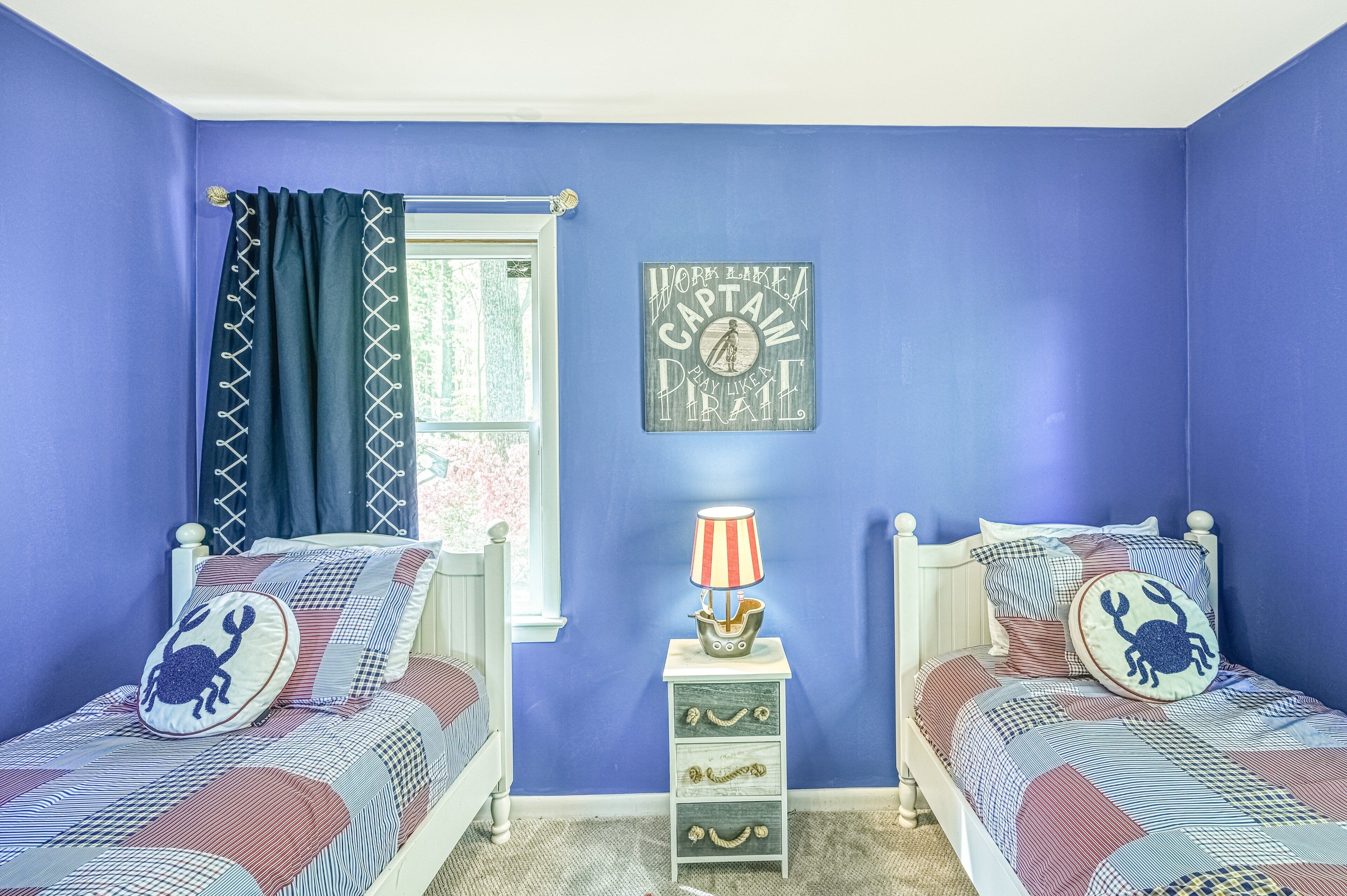 Een slaapkamer met twee bedden, een raam met gordijnen, een nachtkastje met een lamp en een decoratie aan de muur.
