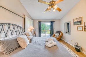 A bedroom with a bed, a ceiling fan, a window with curtains, a chair, and a wall with framed pictures. - Lakefront Adventure House With Private Dock & Wifi - Dog-friendly (Bumpass)