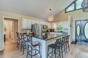 A modern kitchen with white cabinets, a large island with bar stools, and a hanging light fixture. - Lakefront Adventure House With Private Dock & Wifi - Dog-friendly (Bumpass)