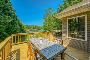 A wooden deck with a table and chairs, overlooking a swimming pool and lush greenery. - Lakefront Adventure House With Private Dock & Wifi - Dog-friendly (Bumpass)