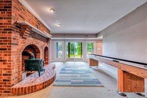 A room with a brick fireplace, a pool table, and a view through glass doors. - Lakefront Home in Private Location With Dock, Firepit, Game Room & Pickleball (Mineral)