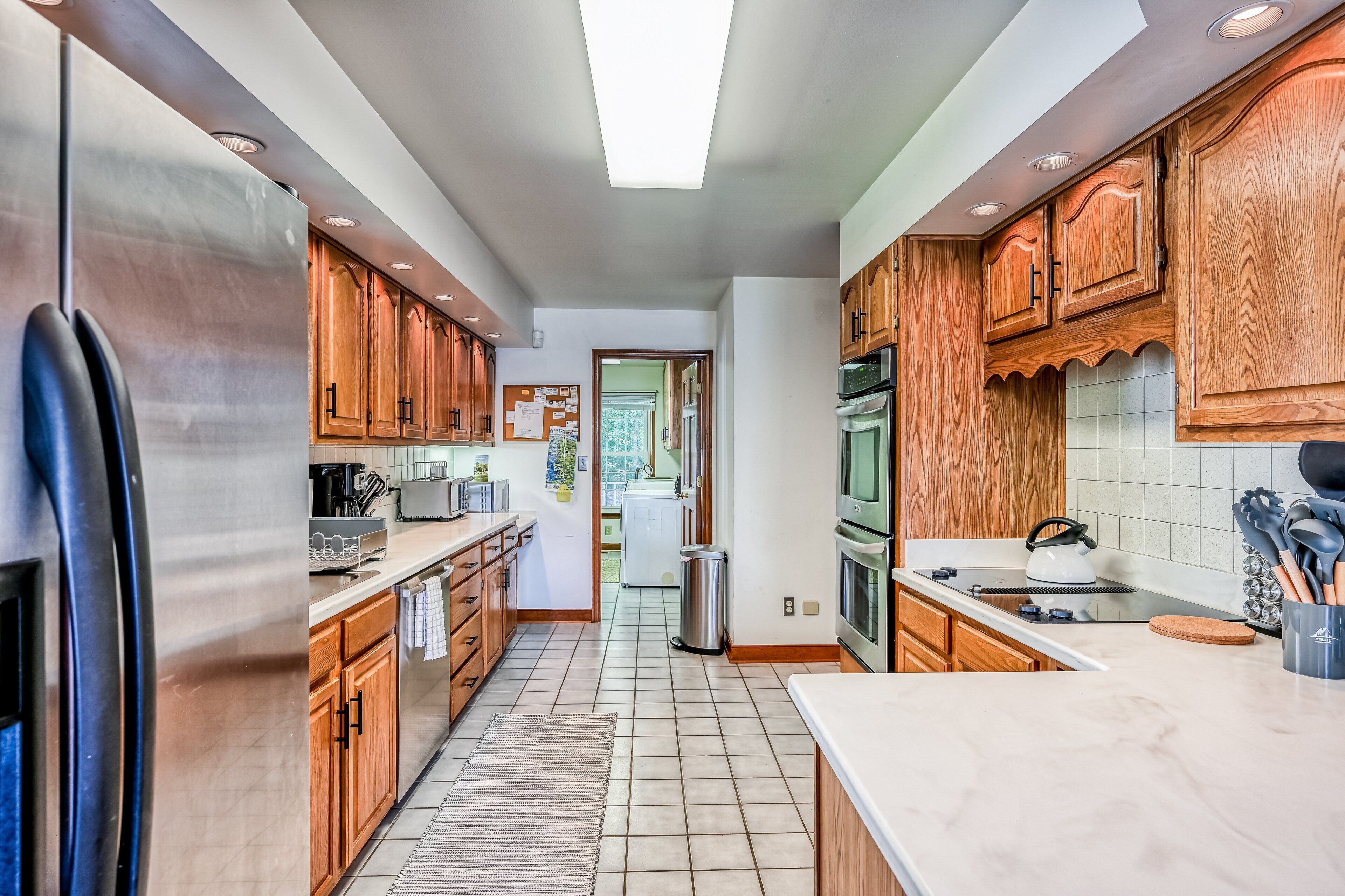 A modern kitchen with wooden cabinets, stainless steel appliances, and a tiled floor.