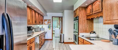A modern kitchen with wooden cabinets, stainless steel appliances, and a tiled floor.