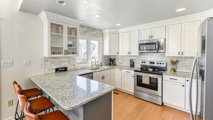 Eine moderne Küche mit weißen Schränken, einer Granit Arbeitsplatte, Edelstahlgeräten und einer Bar mit Hockern.