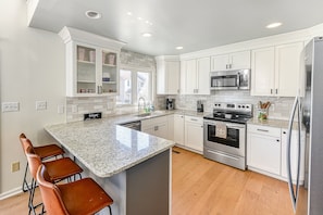 A modern kitchen with white cabinets, a granite countertop, stainless steel appliances, and a bar area with stools. - Three-story Lakefront Home w/ Covered Boat Slip, and Tennis/pickleball Access (Mineral)