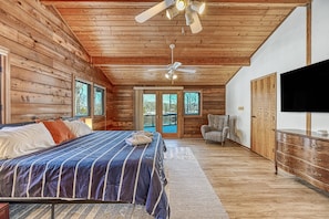 A log cabin bedroom with a bed, ceiling fans, a TV, and a view through the glass doors. - Lakefront Retreat W/private Dock, Fast Wifi, gas Grill & Central AC, Dogs (Mineral)