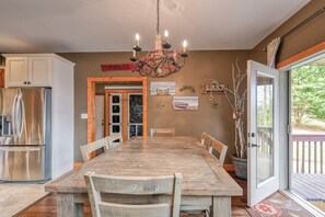Un comedor con mesa de madera, sillas, una araña y vistas al exterior.