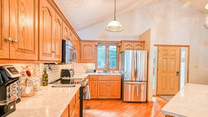 A kitchen with wooden cabinets, stainless steel appliances, and a marble countertop. - Lakefront Home With Deck, hot Tub, Game Room, Kayaks, & Fireplace (Bumpass)