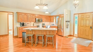 A kitchen with wooden cabinets, stainless steel appliances, and a central island with stools. - Lakefront Home With Deck, hot Tub, Game Room, Kayaks, & Fireplace (Bumpass)