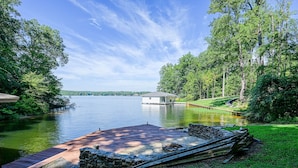 A lakeside property with a dock, stone walls, and a small building. - Lakefront Home With Deck, hot Tub, Game Room, Kayaks, & Fireplace (Bumpass)