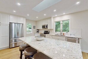 A modern kitchen with white cabinetry, stainless steel appliances, a granite countertop, and a large window. - Spacious Waterfront Escape With Screened Porch, Water Slide, Kayak, & Games (Mineral)