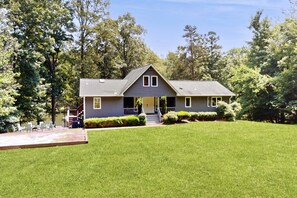 A house with a front porch, a lawn, and trees in the background. - Spacious Waterfront Escape With Screened Porch, Water Slide, Kayak, & Games (Mineral)