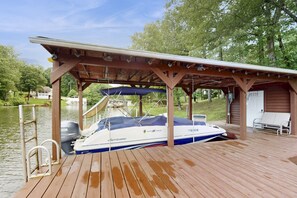 A boat docked at a wooden pier with a covered seating area and a small building in the background. - Spacious Waterfront Escape With Screened Porch, Water Slide, Kayak, & Games (Mineral)
