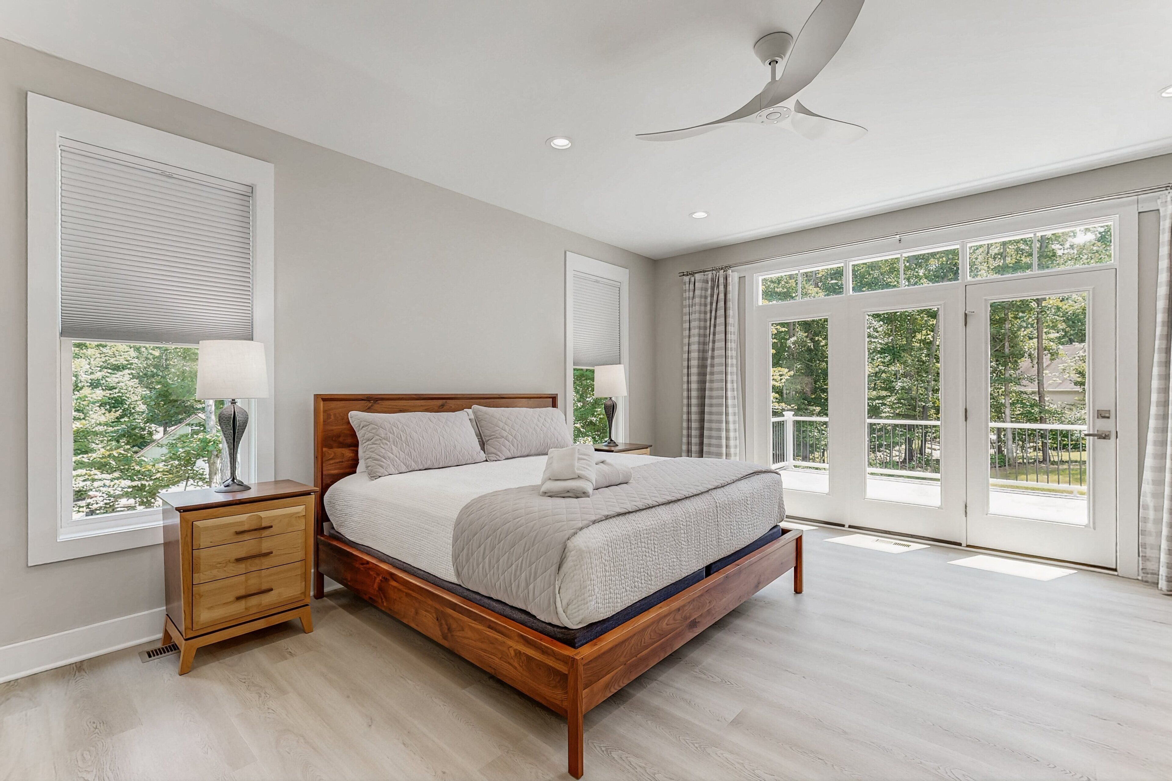A bedroom with a wooden bed, a nightstand, a ceiling fan, and large windows.