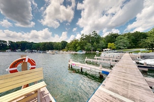 A wooden dock extending into a lake with boats docked, surrounded by trees and a clear sky.