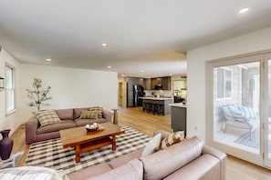 Ein modernes Wohnzimmer mit einer Couch, einem Couchtisch und Blick auf Küche und Terrasse.