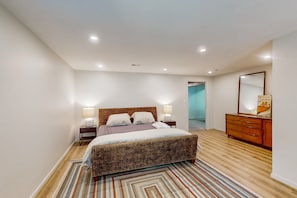Ein Schlafzimmer mit einem großen Bett, einer hölzernen Kommode, einem Spiegel und einer Tür zu einem anderen Raum.