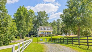 A house with a gravel driveway, surrounded by a wooden fence and lush greenery. - Lakeview Escape Near Beach With Fenced dog Run, Porch & Dock With one Boat Slip (Louisa)