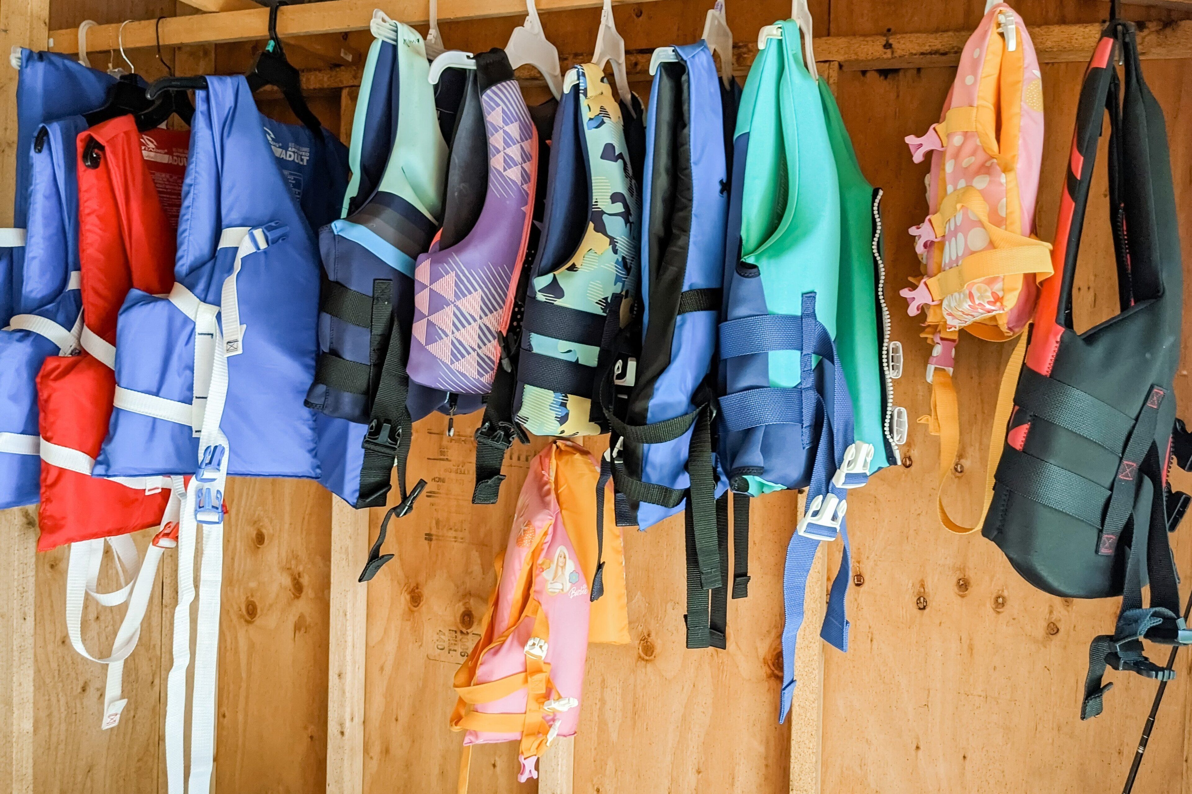 Diverse Rettungswesten und ein Rucksack hängen an einer Holzwand.