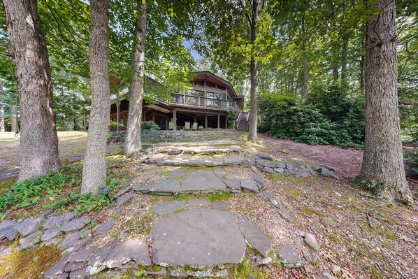 A stone pathway leading to a wooden cabin surrounded by trees. - Lakefront Escape With Private Docks, Three-season Room, and Spacious Bunk Room (Mineral)