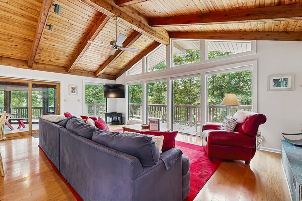 A spacious living area with a large gray sofa, a red armchair, and a wooden ceiling with exposed beams. - Lakefront Escape With Private Docks, Three-season Room, and Spacious Bunk Room (Mineral)