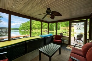 Un espacio al aire libre techado con ventilador de techo, una mesa, sillas y vistas a un lago y un muelle.