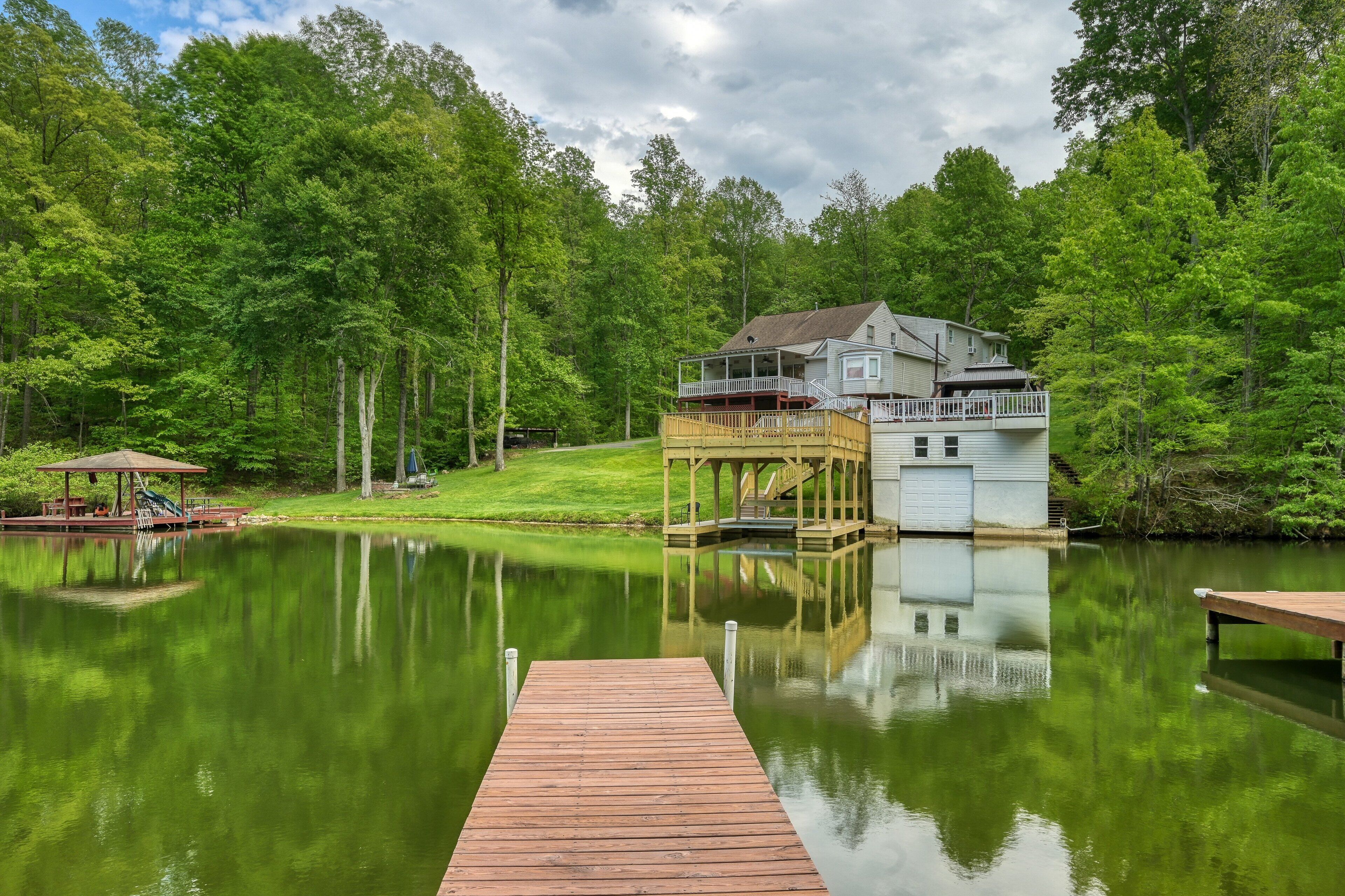 A lakeside property with a dock, a covered deck, and a house with a second level.