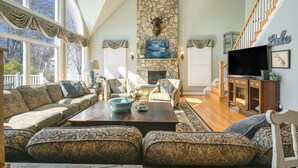 A living room with a stone fireplace, a large window, a sofa set, and a television. - Large Lakefront Home on the Best Part of the Lake Spacious With Stunning Views (Bumpass)