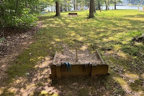 A wooden bench in a grassy area with a lake and trees in the background. - Relaxing Lakeside Retreat With Boathouse, Dock, Deck, Firepit and Screened Porch (Bumpass)