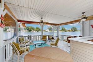 A covered outdoor area with a table and chairs, a ceiling fan, and a view of a body of water. - Relaxing Lakeside Retreat With Boathouse, Dock, Deck, Firepit and Screened Porch (Bumpass)