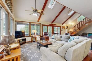 A spacious living room with a large couch, a television, and a ceiling fan. - Relaxing Lakeside Retreat With Boathouse, Dock, Deck, Firepit and Screened Porch (Bumpass)