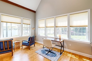 A room with a wooden floor, a desk with a chair, a blue armchair, and large windows with blinds. - Lakefront Home With Private Dock, Kayaks, Beach, Badminton, Firepit, & Deck (Mineral)